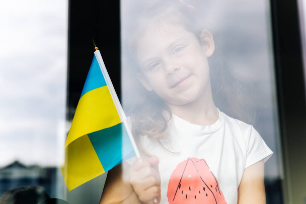 girl with the flag of ukraine in her hands looks out the window - Foto, immagini