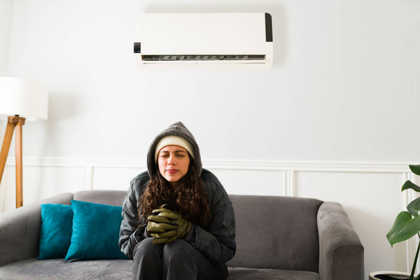 Mujer hispana fría enfriándose en la sala de estar. Hermosa mujer con una chaqueta caliente mientras el aire acondicionado está encendido - Foto, Imagen