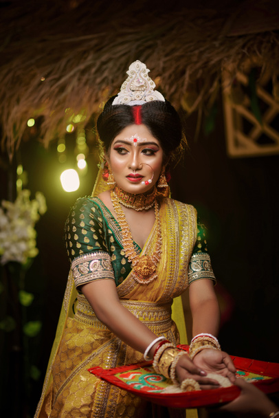 Close-up portret van een zeer mooie Bengali bruid in gele banarasi saree, gouden sieraden en met een prachtige expressie.  - Foto, afbeelding