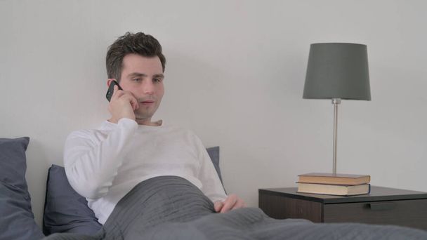 Ο άνθρωπος που μιλάει για κλήση στο Smartphone στο κρεβάτι - Φωτογραφία, εικόνα