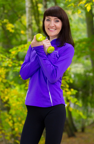 Brunette during fitness exercise with dumbbells in autumn park - Fotó, kép