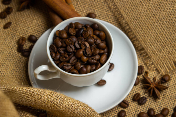 Una taza llena de granos de café. Granos de café tostados en arpillera. - Foto, Imagen