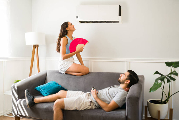 Sad woman feeling hot and trying to cool down sitting below the air in the ac unit with her partner  - Foto, Imagen
