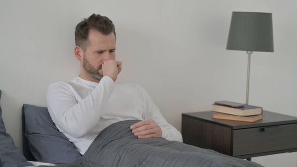 ベッドで寝ている間に男が咳をする - 写真・画像