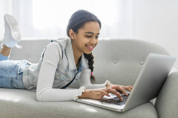 An African Teen Girl Using Laptop Computer Browsing Internet Sitting On Couch At Home - Φωτογραφία, εικόνα
