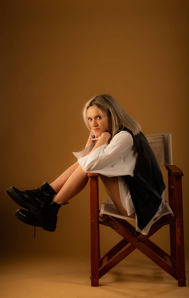 Aantrekkelijk en verbazingwekkend jong meisje poseert op de stoel alleen op gele achtergrond in de studio - Foto, afbeelding