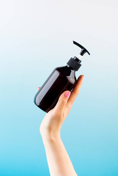 Mockup of a brown dispenser with a natural cosmetic product in a female hand on a blue background. - Fotoğraf, Görsel