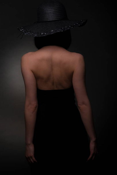 Elegant girl is posing from the back in black dress, in studio - Photo, Image