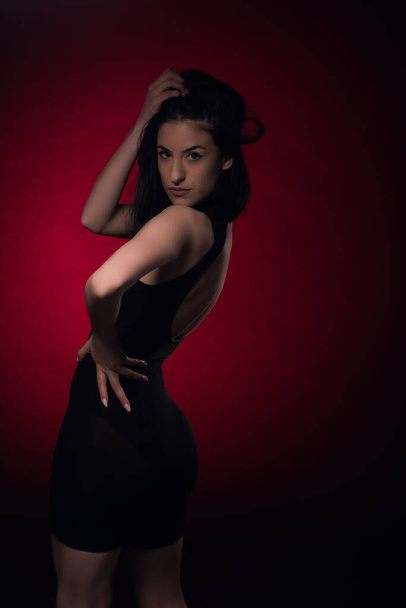Chica seductora y atractiva está posando desde la espalda sobre fondo rojo, en el estudio - Foto, Imagen
