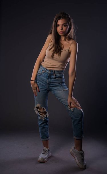 Studio body shot d'une mannequin féminine posant dans des vêtements modernes isolés sur un mur sombre - Photo, image