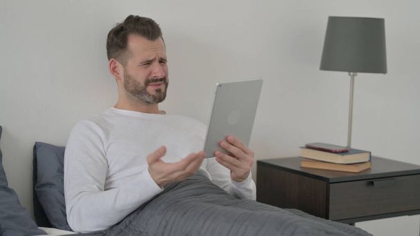 Man Reacting to Loss on Tablet in Bed - Фото, зображення