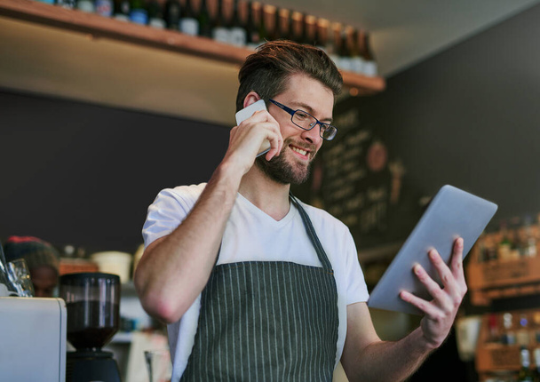Let me confirm that. Shot of a young barista taking orders via cellphone and logging them on his tablet. - 写真・画像
