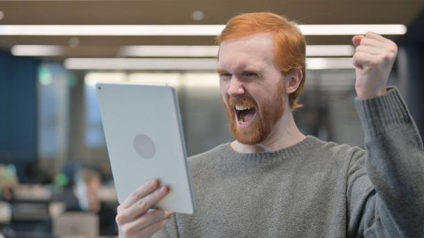 Jeune homme célébrant sur tablette numérique au bureau  - Photo, image