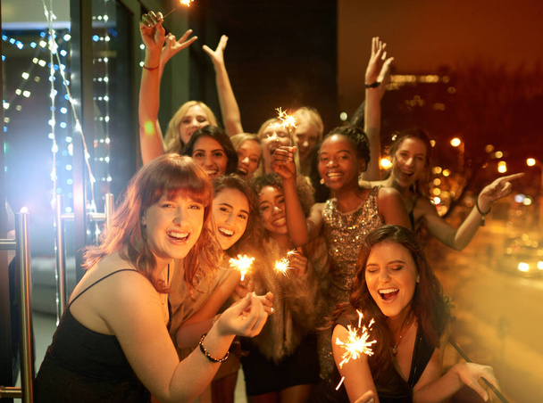 Αστραφτερή στην Πρωτοχρονιά. Πυροβολισμός μιας ομάδας φιλενάδων που διασκεδάζουν με βεγγαλικά στο μπαλκόνι μια νύχτα έξω.. - Φωτογραφία, εικόνα