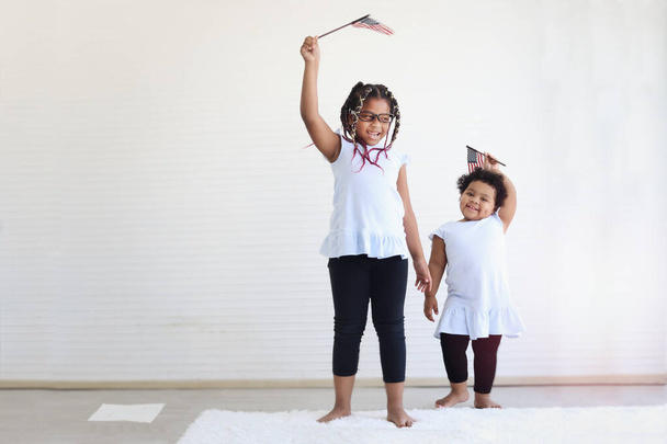 Two African American girl sisters holding and waving American flag in indoor living room on 4th July to celebrate national Independence Day, Flag Day concept - Фото, зображення