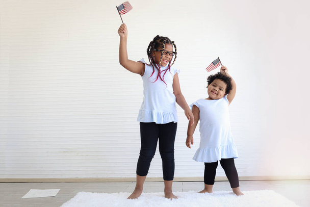 Two African American girl sisters holding and waving American flag in indoor living roo - Photo, Image