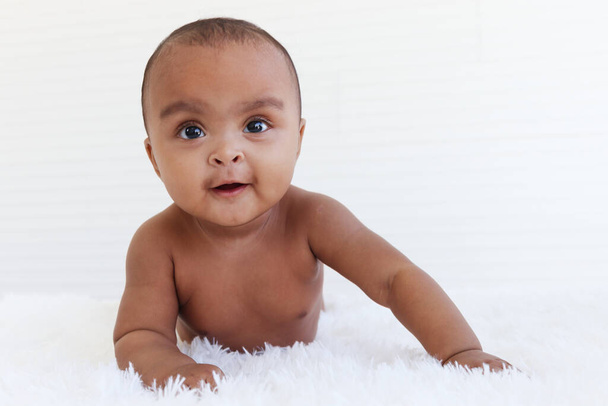 Portret sześciomiesięcznego, pełzającego Afroamerykańskiego dziecka na puszystym białym dywanie, uśmiechniętego, uroczego, słodkiego dziecka leżącego na łóżku w sypialni, dzieciństwie i koncepcji opieki nad dzieckiem - Zdjęcie, obraz