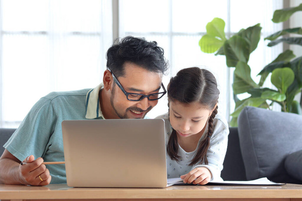 Young handsome father teach adorable girl daughter to do school homework, using laptop computer for e-learning study at home, dad and kid spend time together for education and searching Internet. - 写真・画像