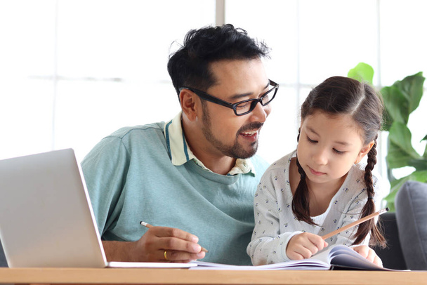 Młody przystojny ojciec uczyć uroczą córkę do pracy domowej szkoły, za pomocą laptopa do e-learningu w domu, tata i dziecko spędzają razem czas na edukację i wyszukiwanie Internetu. - Zdjęcie, obraz