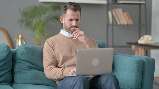 Человек с ноутбуком мыслит на диване  - Фото, изображение
