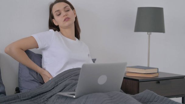背中の痛みを持つ女性はベッドでノートパソコンで作業 - 写真・画像