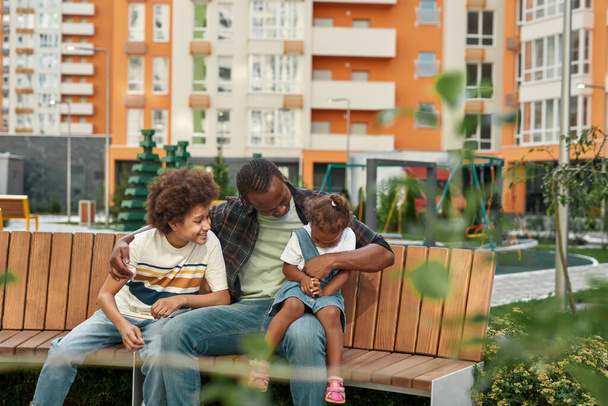 Black family sit and rest on bench in city yard - Фото, изображение