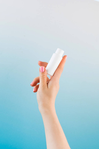 Banner a womans hand holds a white tube with a cosmetic product on a blue.  - Foto, afbeelding