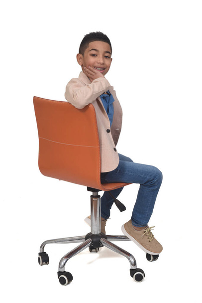 side view of a boy sitting a chair turned and hands on face on white background - Photo, Image