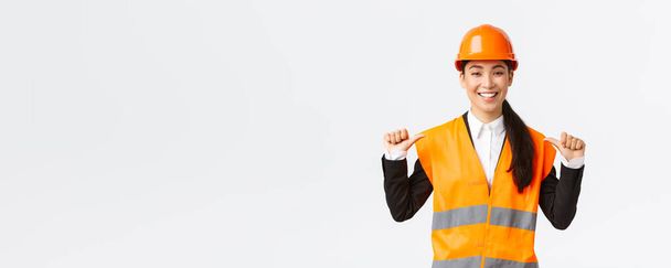 Exitosa orgullosa sonriente asiática gerente de construcción, ingeniera en casco de seguridad señalándose a sí misma, presumiendo. Arquitecto recomienda asistencia personal, alardear logros
 - Foto, imagen