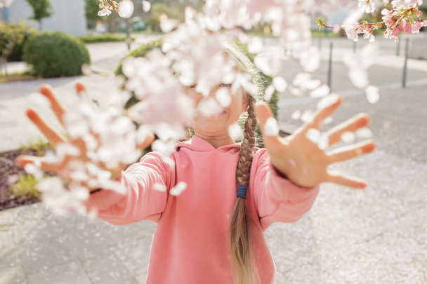 Ένα κορίτσι απολαμβάνει άνθη σακούρα, ενώ περπατά μέσα από το περιβόλι κεράσι την άνοιξη - Φωτογραφία, εικόνα