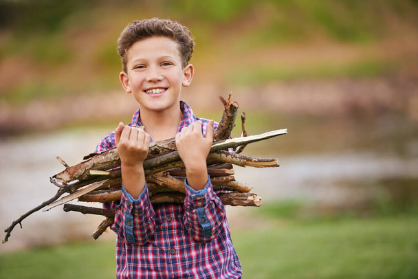 Es suficiente madera. Retrato de un niño llevando un manojo de palos para un fuego mientras acampaba. - Foto, imagen