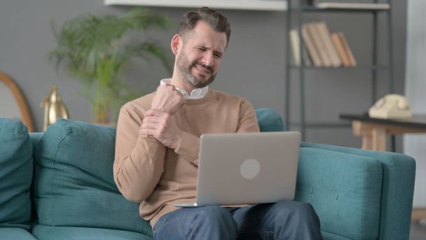 Man met laptop met polspijn op de bank  - Foto, afbeelding