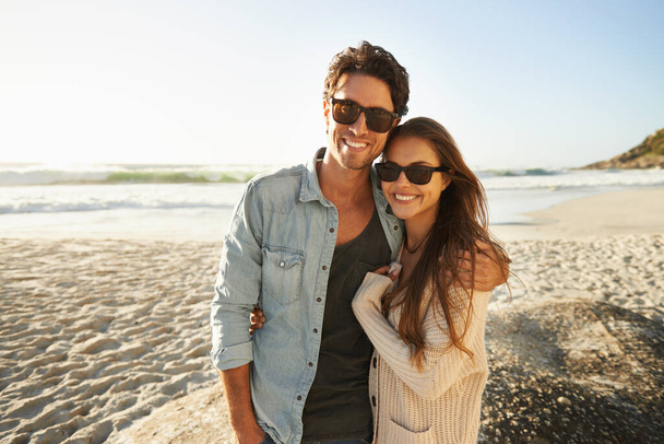 Disfrutando de la brisa del mar y el sol. Foto de una hermosa pareja joven de pie lado a lado en la playa. - Foto, imagen