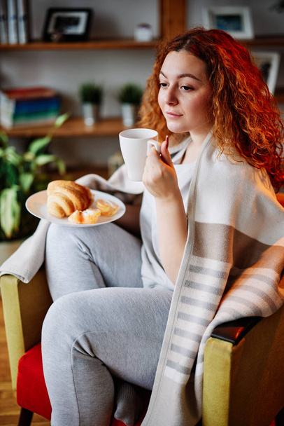 Słodka młoda kobieta z czerwonymi kręconymi włosami cieszy się rano filiżanką kawy. - Zdjęcie, obraz