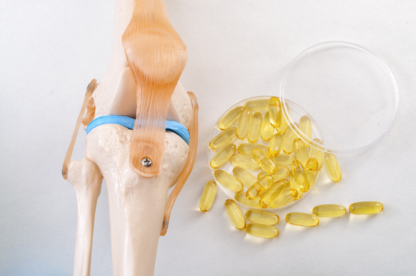 Salute articolare, acidi grassi omega 3 sani e ridurre il concetto di infiammazione dell'artrite con plastico modello di insegnamento medico di un ginocchio umano e pillole di olio di pesce isolato su sfondo bianco - Foto, immagini