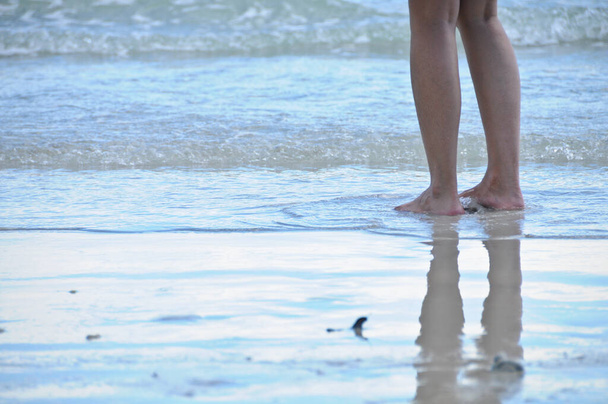Two legs of lady standing on sandy wet beach of the sea with reflection - Фото, изображение