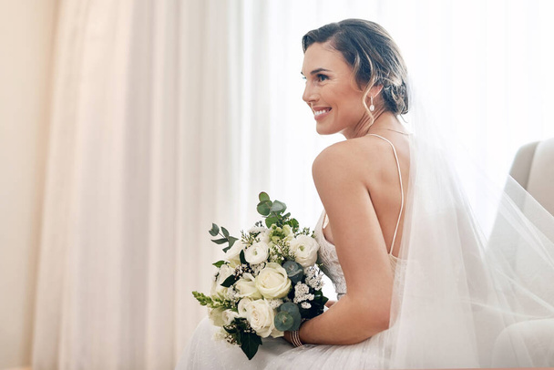 Stralend mooi op haar trouwdag. Gehakt schot van een aantrekkelijke jonge bruid zit alleen in de kleedkamer en houdt haar boeket bloemen. - Foto, afbeelding