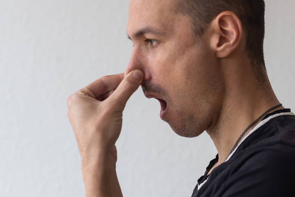 Man smells something stinky and pinches his nose to stop the bad odor - Photo, Image
