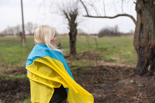 mujer bandera de Ucrania cerca de árbol quemado - Foto, imagen