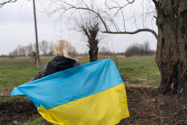 Frau mit gelb-blauer Flagge der Ukraine auf dem Hintergrund eines verbrannten Baumes - Foto, Bild