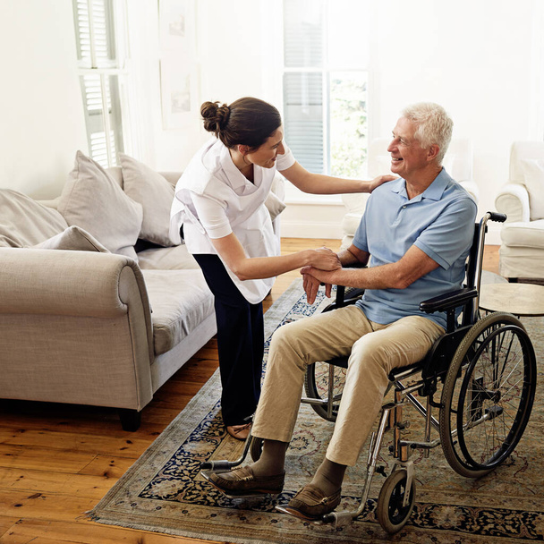 Altenpflege ist ihre Berufung. Aufnahme einer Pflegerin, die einem älteren Mann im Rollstuhl zu Hause hilft. - Foto, Bild
