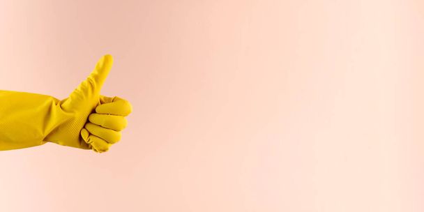 A hand in a yellow rubber glove for washing and cleaning shows a thumbs up. Copy space. Banner - Foto, afbeelding