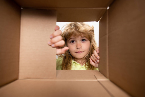 Surprised child boy unpacking, opening carton box and looking inside. The package, delivery, surprise, gift for kid. Children emotions and kids facial expressions concepts. - Foto, afbeelding