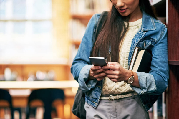 Sejdeme se v knihovně. Detailní záběr studentky univerzity, jak si textuje na mobil v knihovně v kampusu. - Fotografie, Obrázek
