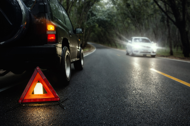 Señal roja de parada de emergencia (señal de advertencia de triángulo rojo) y coche SUV negro roto en la carretera del campo bajo la lluvia de verano. - Foto, Imagen