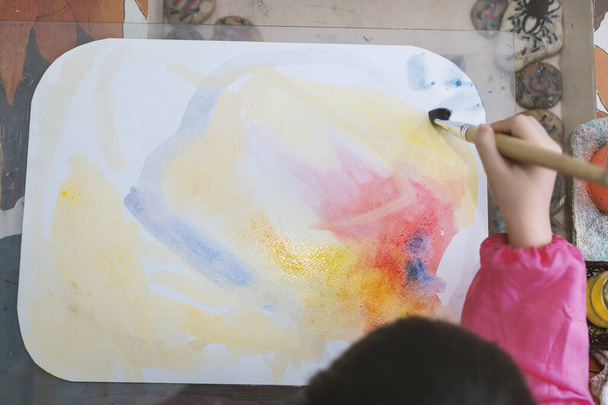Вид сверху на маленькую девочку, рисующую акварелью дома, выборочный фокус - Фото, изображение