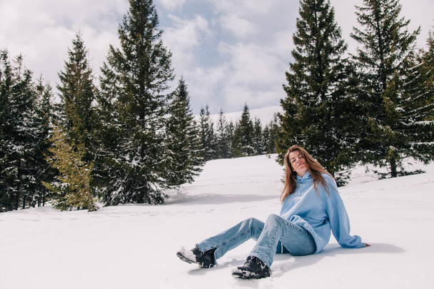 A young, beautiful girl in the mountains sits in the snow among the trees - Photo, image
