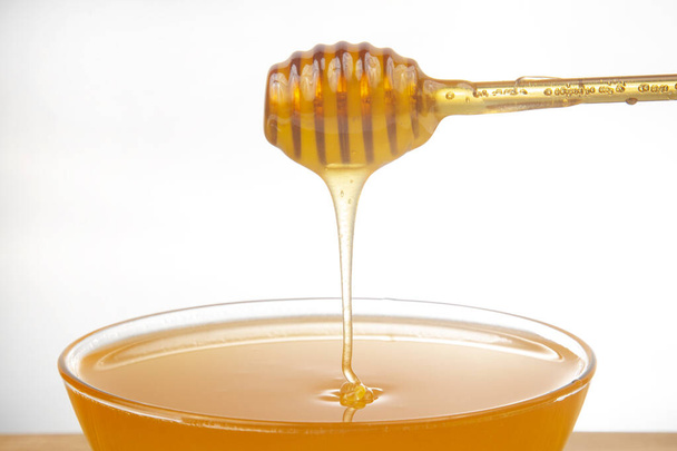 frischer Honig tropft aus einem Löffel in einen transparenten Teller auf weißem Hintergrund. Bio Vitamin Gesundheit Lebensmittel - Foto, Bild