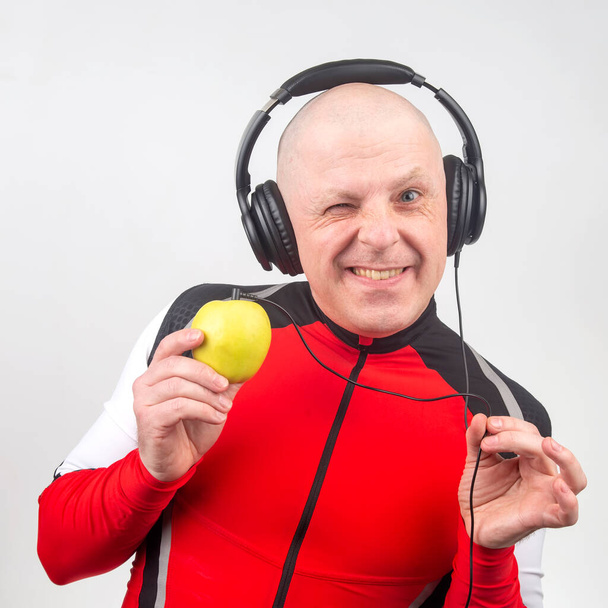 лысый мужчина в наушниках слушает музыку через желтый яблочный плеер. Метафора и концепция витаминов в музыке и звуке - Фото, изображение