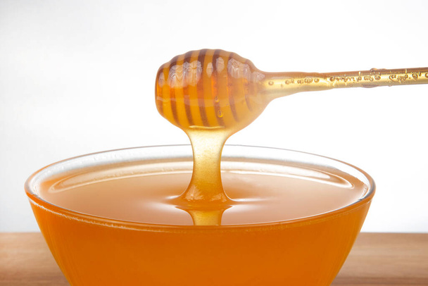 frischer Honig tropft aus einem Löffel in einen transparenten Teller auf weißem Hintergrund. Bio Vitamin Gesundheit Lebensmittel - Foto, Bild